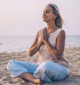 Woman sitting at peace on beach after using functional medicine plan. She is raising her hands in gratitude to her health.